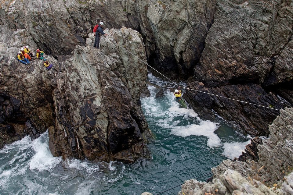 One man takes a zip line across rocks above water