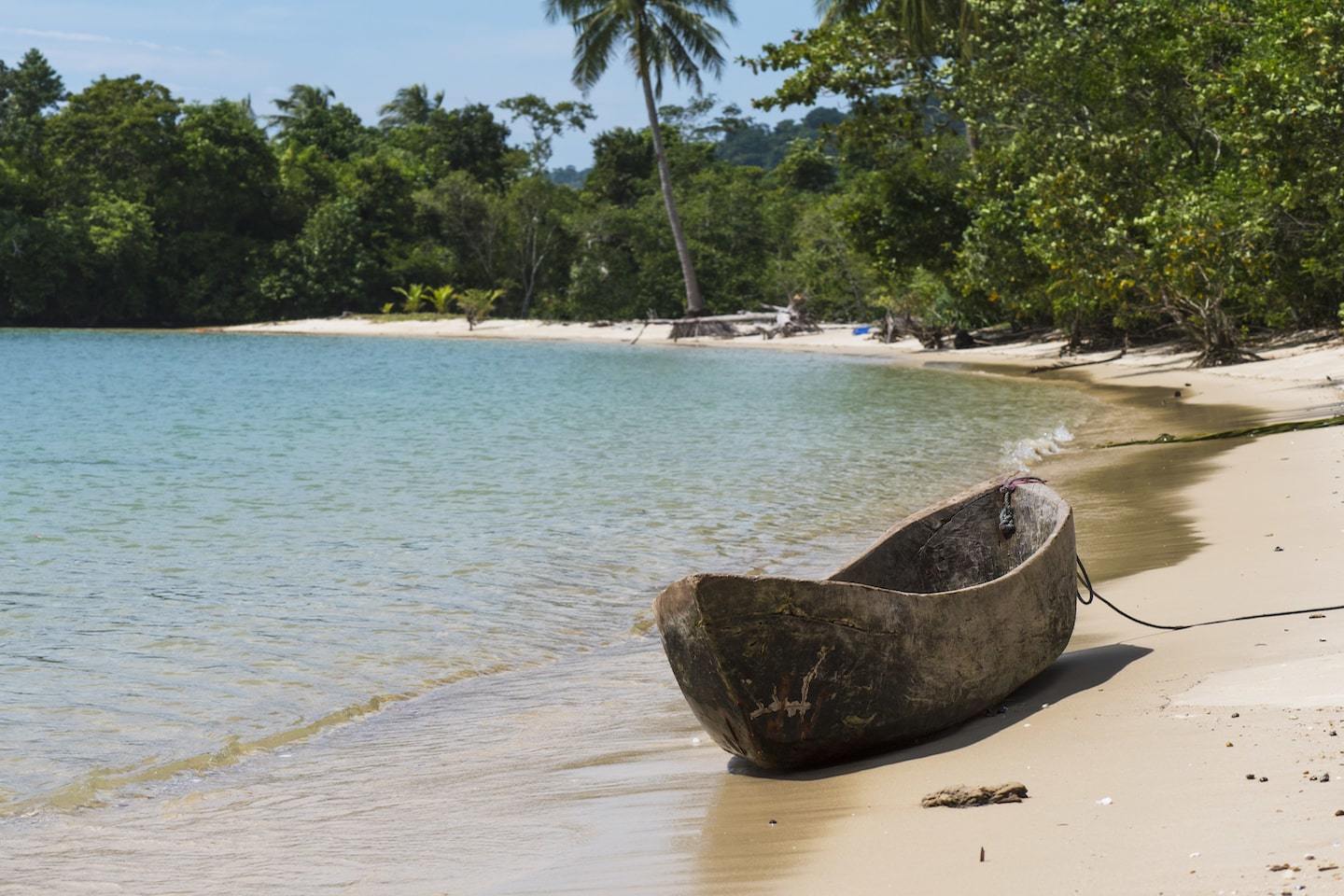 canoe on empty beach in front of forest and clear water