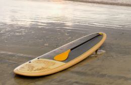 A yellow paddle board and oar on a tropical beach
